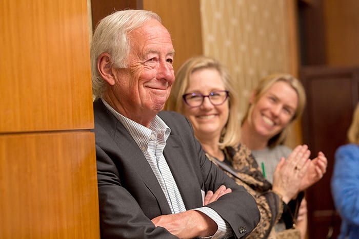 Bob Hill leans against a wall while smiling, he is a bold investor.